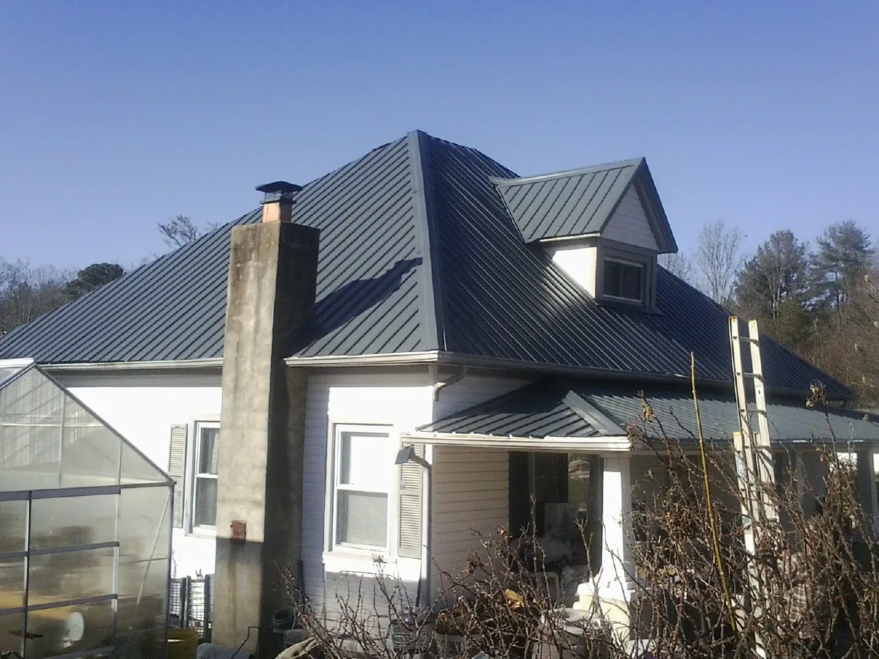 Dark blue standing seam metal roof on a white farmhouse with dormer — Slate & Tile Roof Repair by Roofing Brothers in Osage City
