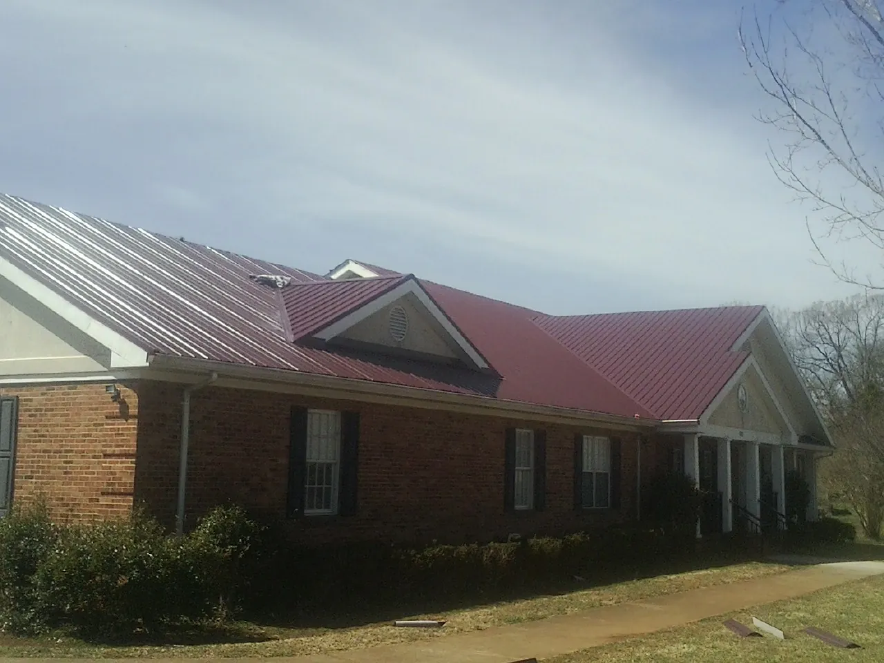 Red metal roof with gabled entries on a long brick building, from a Hail Damage Roof Repair job in Osage City