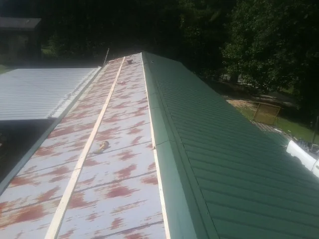 Old rusted panels beside newly installed green metal roofing — Wind Damage Roof Repair by Roofing Brothers in Osage City