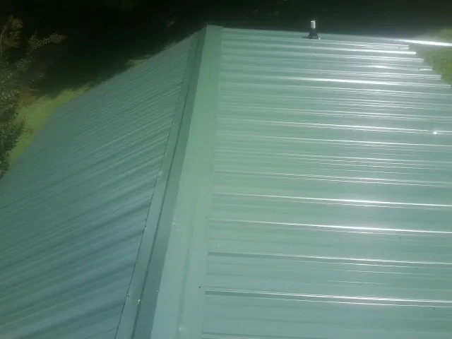 New green metal panels meeting at the ridge of a roof — Flat Roof Repair work by our crew in Osage City