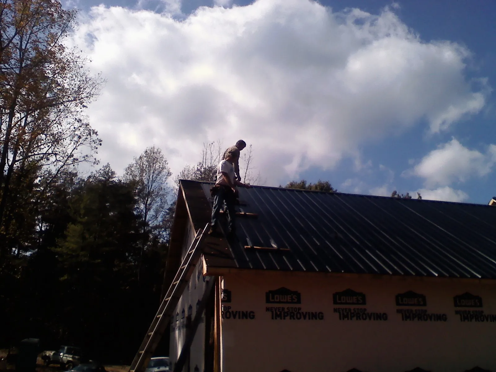 Roofer fastening dark metal panels high against a cloudy sky, from a Roof Inspection job in Osage City