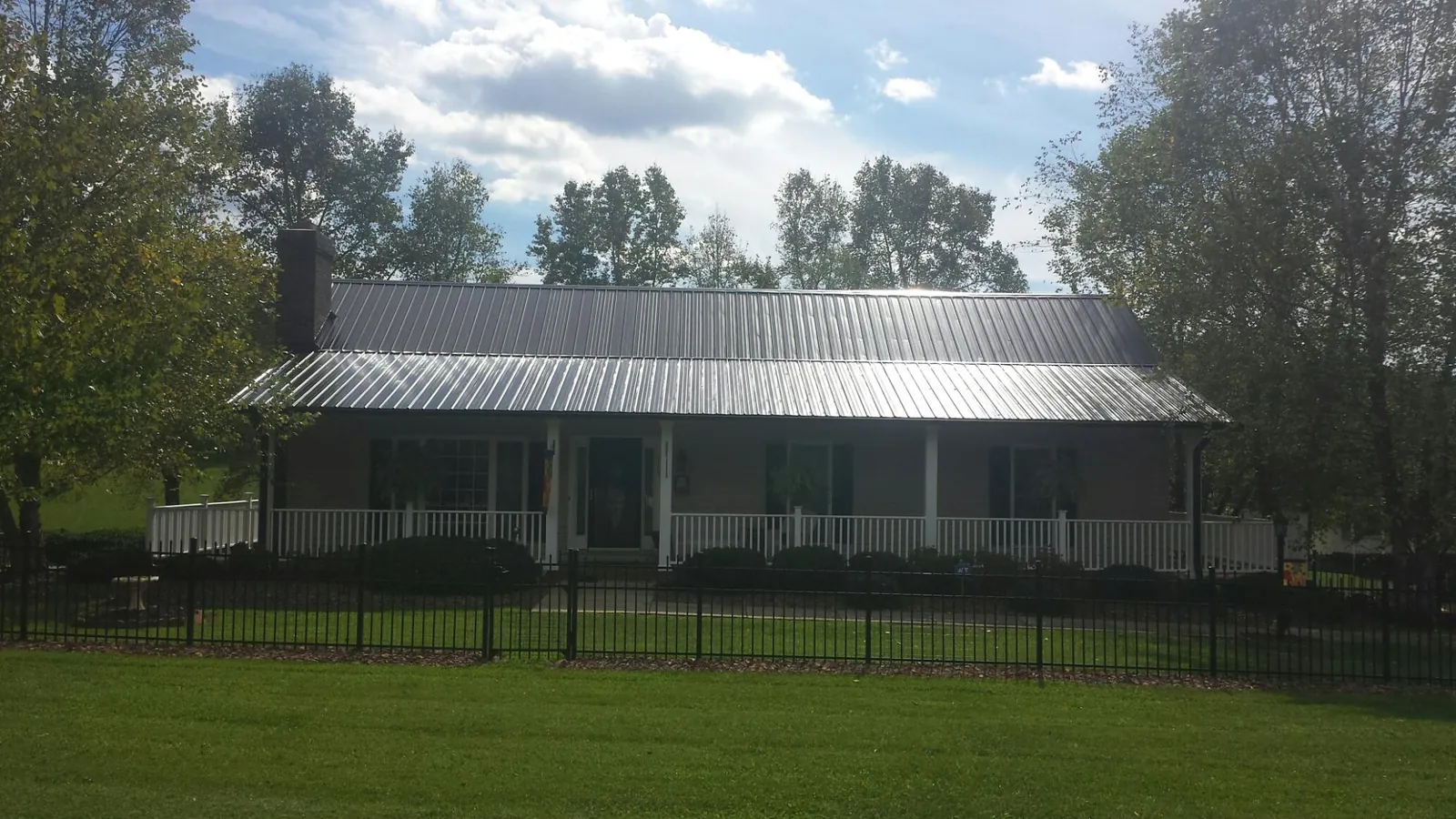 Gray metal roof on a brick ranch with a full width front porch — Gutter Guard Installation work by our crew in Osage City