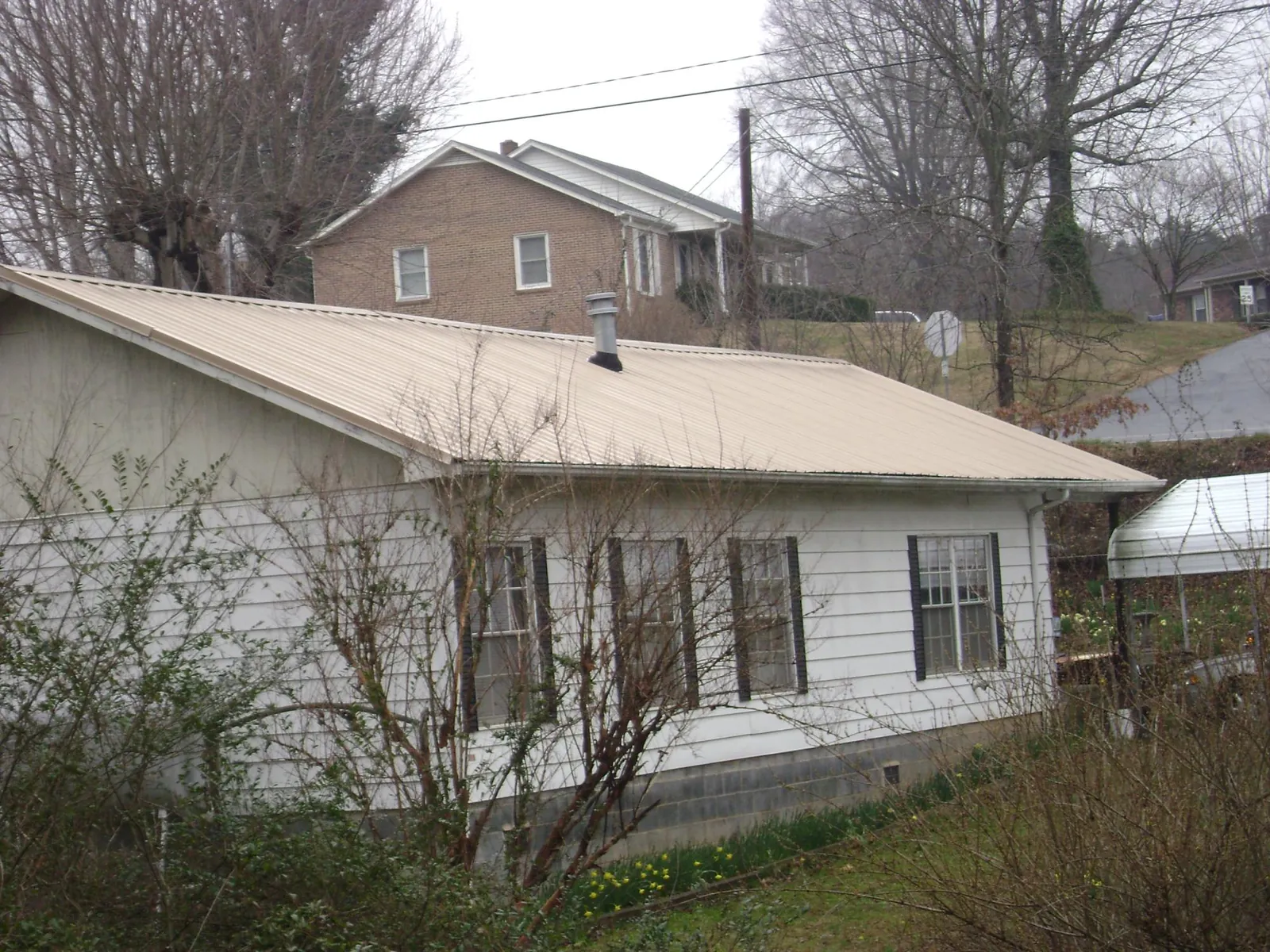 Tan metal roof on a white sided house set into a hillside — Commercial Roofing by Roofing Brothers in Osage City