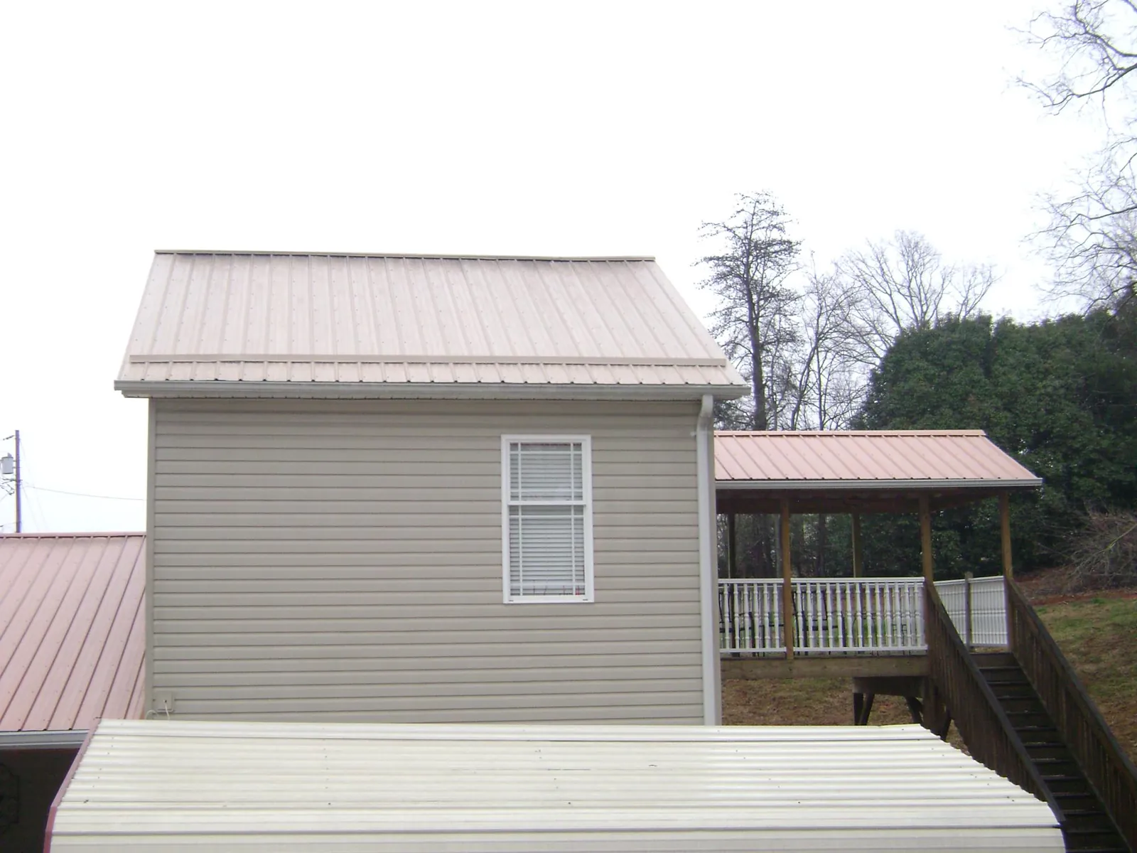 Tan metal roofs on a two story addition and attached porch, from a Roof Replacement job in Osage City